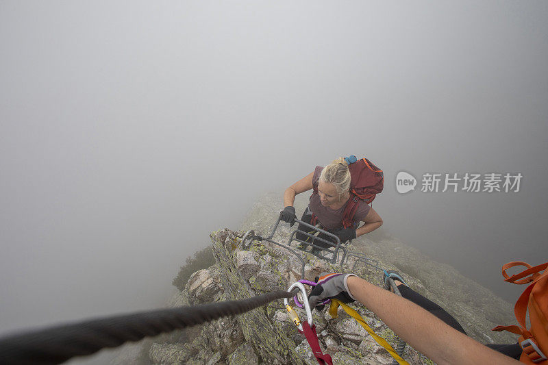 在雾中，一名年轻女子爬上via ferrata